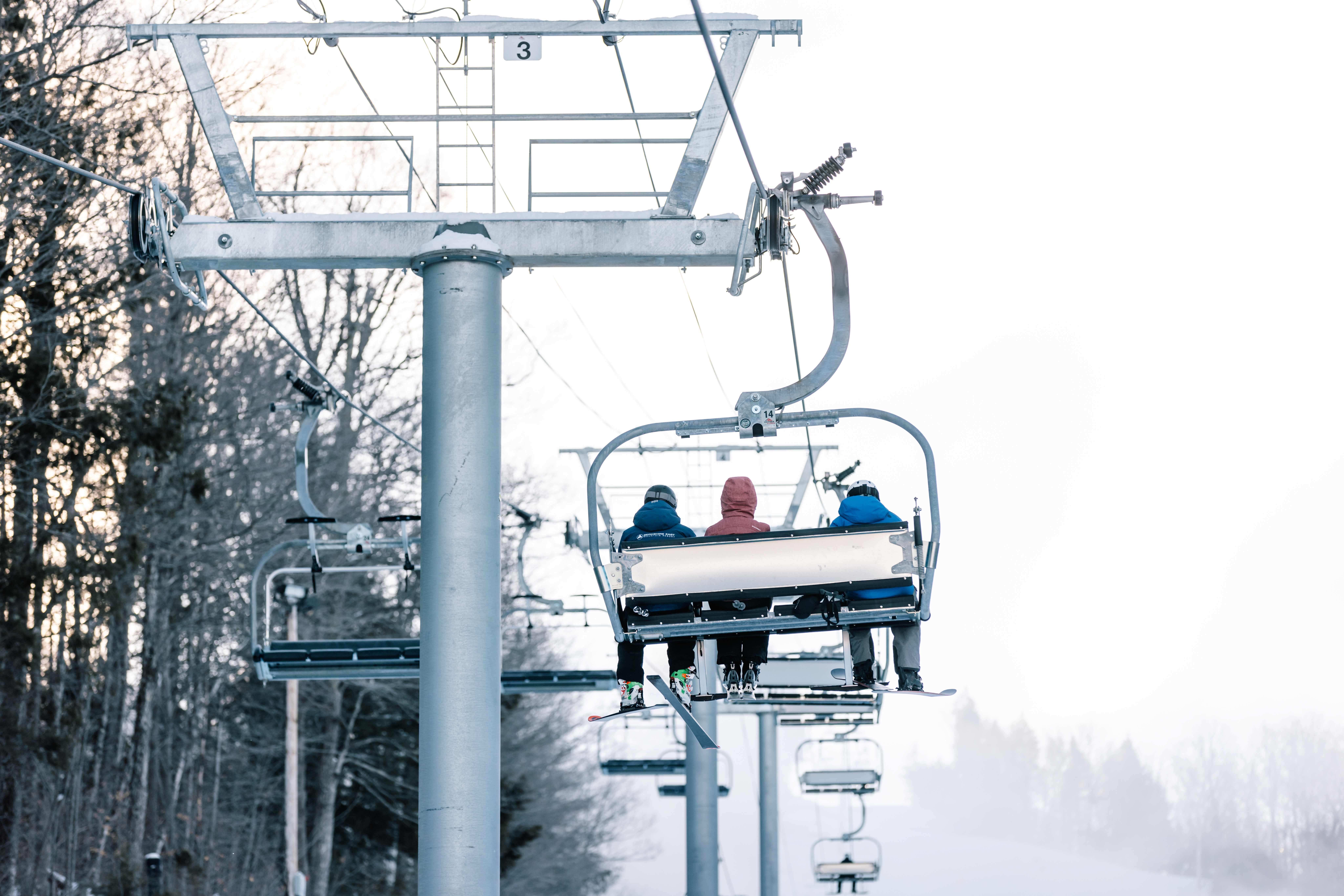 Three Skiers on a chairlift, view from the back.